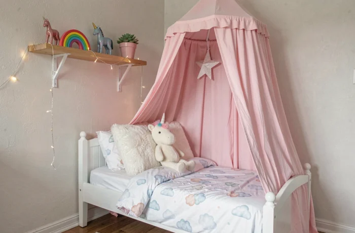 Chambre d'enfant décorée sur le thème licorne avec baldaquin rose, peluche et étagère décorative