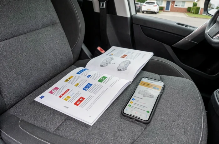 Manuel du propriétaire Peugeot 208 ouvert sur une page de symboles du tableau de bord avec smartphone